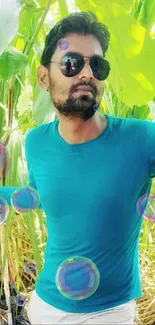 A man in sunglasses with a teal shirt amidst lush green leaves.