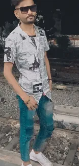 Man in urban outfit stands on railroad track at night.