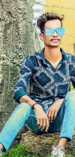 Young man in denim with trendy glasses sitting outdoors.