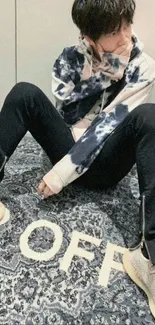 Styled individual in urban fashion sitting on a patterned carpet in modern wallpaper.