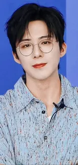 Young man with glasses in a blue shirt on a blue background.