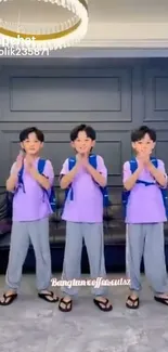 Three children in matching outfits standing indoors in a modern living room.