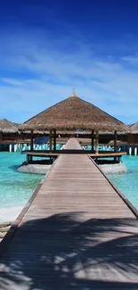 Wooden walkway leading to huts over turquoise ocean with blue sky.