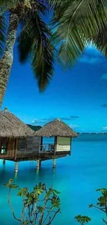 Tropical beach scene with palm trees and overwater huts under blue sky.