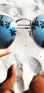 Sunglasses reflecting palm trees on a sandy beach.