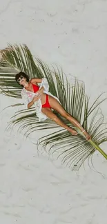 Woman in red swimsuit on palm leaf on beach.