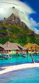 Tropical island with bungalows surrounded by clear blue water and lush mountains.