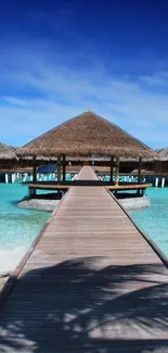 Wooden path leading to thatched huts over turquoise water under a blue sky.