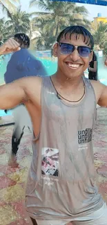 Smiling person flexing by a tropical pool.