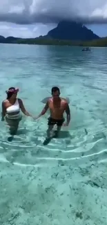 Couple strolling in turquoise waters with island backdrop.