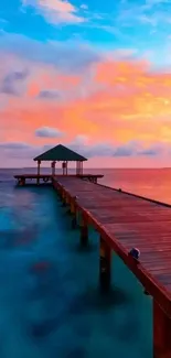 Wooden dock extending into vibrant ocean at tropical sunset