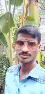 Man in sunglasses under banana leaves in a lush environment.