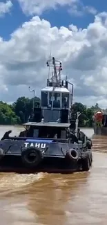 Tugboat moving through a muddy river against a bright blue sky.