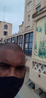 Man with mask in front of mural on urban building.