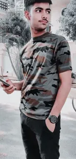 Man in camouflage shirt holding a phone, standing outdoors.