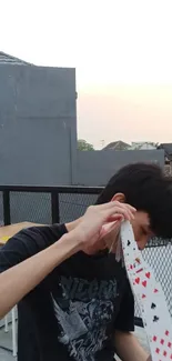 Youth performing a card trick on a city rooftop at sunset.