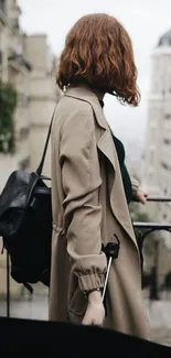 Person in a trench coat with a backpack in a city setting.