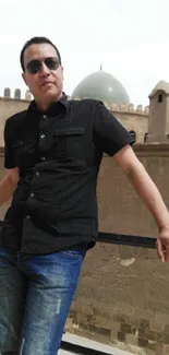 Man in black shirt standing on a rooftop with historic backdrop.