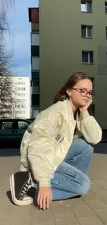 Young person in casual urban outfit posing by a city building.