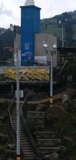 Urban hilltop view with stairs and blue tower in lush greenery.