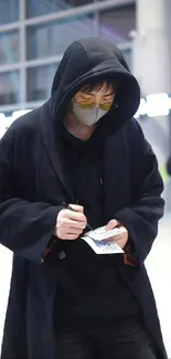 Person in hooded coat writing in an urban setting.