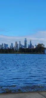 Urban lakeside with city skyline under a bright blue sky.