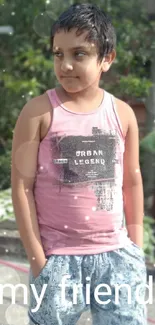 Boy in pink tank top, outdoor setting, lush background.