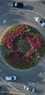 Aerial view of a roundabout with vibrant pink flowers and bustling urban traffic.