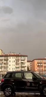 Black car with buildings under a gray sky.