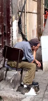 Man sitting on chair with cat on urban street corner.