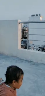 Child on rooftop overlooking urban skyline.