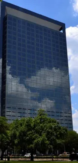 Modern skyscraper amidst green trees and blue sky.