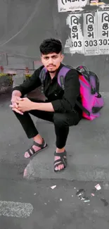 Man sitting on sidewalk in urban style with pink backpack.