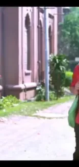 Stylish person walks by brick building on a sunny green street.