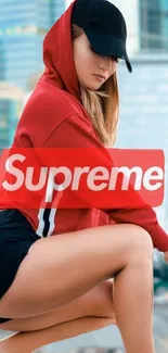 Stylish person in red Supreme hoodie with urban backdrop.