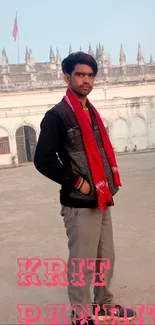 Stylish individual posing in front of a historic building, wearing a red scarf.