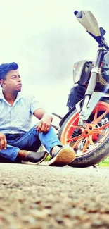 Man sitting by a motorcycle with vibrant wheels on a scenic road.