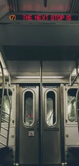 Interior of a subway train with metal doors and neon sign overhead.