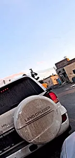 White Land Cruiser on urban street with buildings and blue sky.