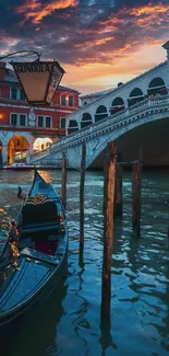 Venetian gondola at sunset with vibrant sky and historic bridge.