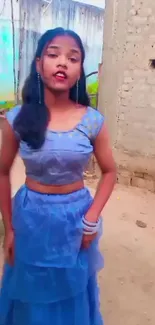 Young woman in blue dress against rustic backdrop.