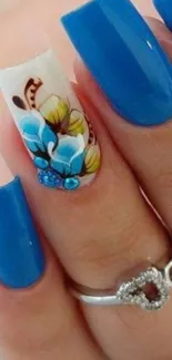 Vibrant blue nail art with floral design on a woman's finger.