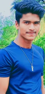 Young man in blue shirt, green outdoor background.