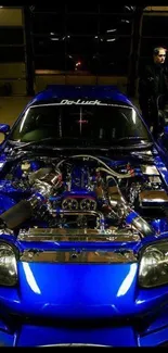 Vibrant blue sports car with exposed engine in a garage setting.