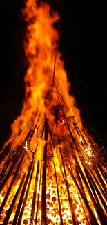 Tall bonfire with bright orange flames against a dark background.