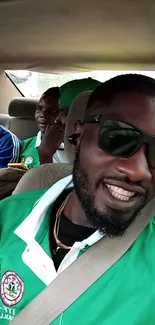 Friends in green shirts smiling during a car ride selfie.