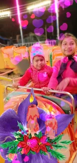 Two kids enjoy a colorful carnival ride with lights and flowers.