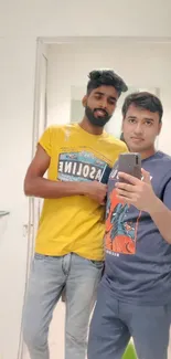 Two men in casual wear taking a selfie in front of a mirror.