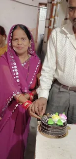 Couple celebrating with a cake, wearing traditional attire.