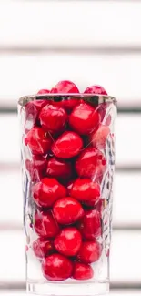 Glass filled with vibrant red cherries against a striped background.